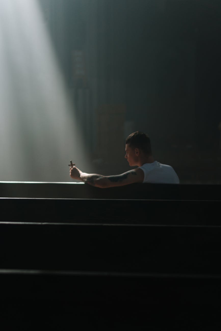 a man in white tank top sitting on a pew while holding a cross